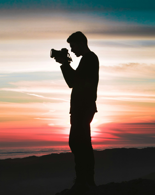 Silhouette of man holding camera in a sunset.